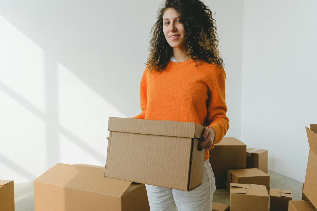 young female arranging carton box and smiling at camera during relocation